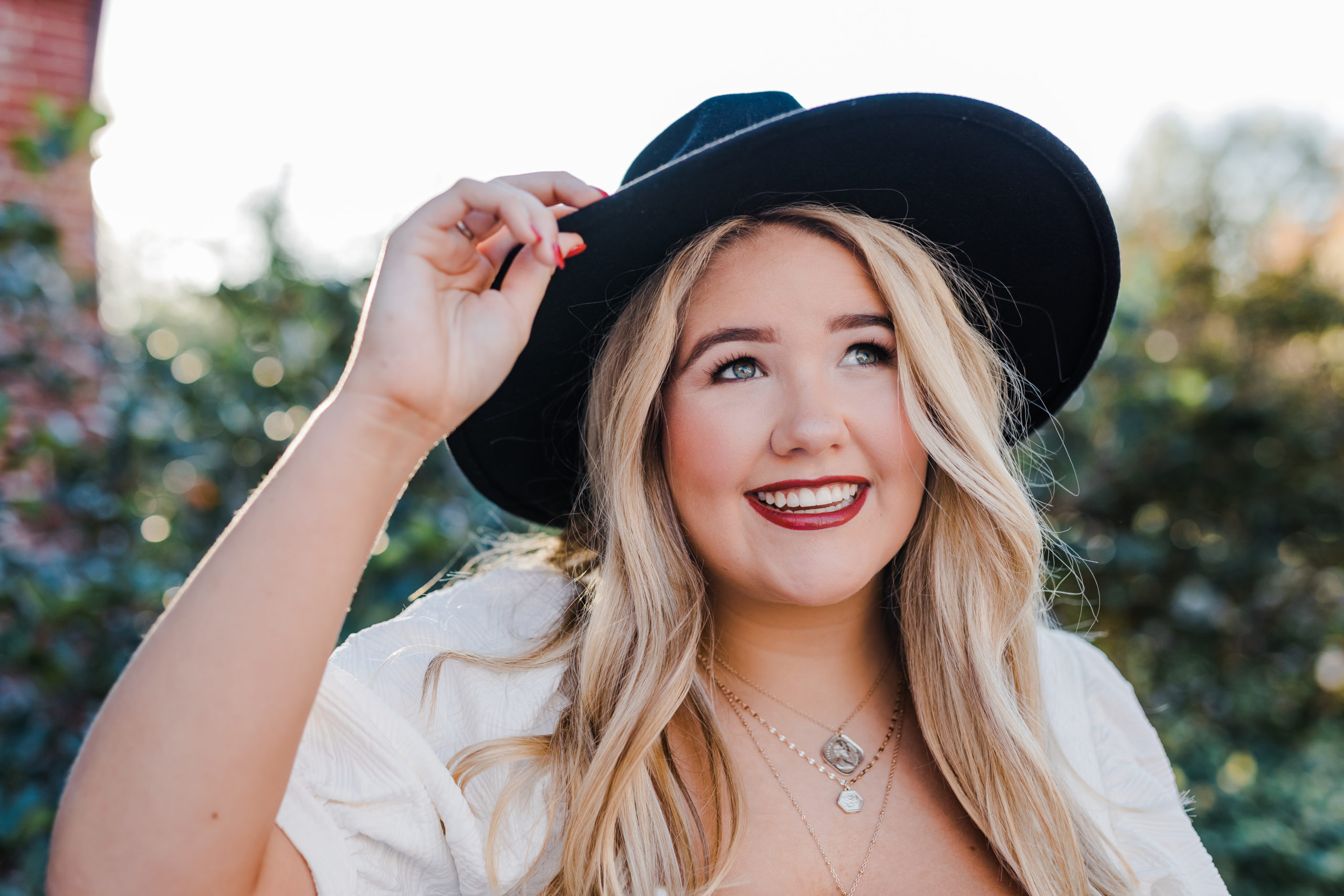 outdoor senior portrait of girl in a white dress and black hat for her downtown senior pictures with Augusta photographer