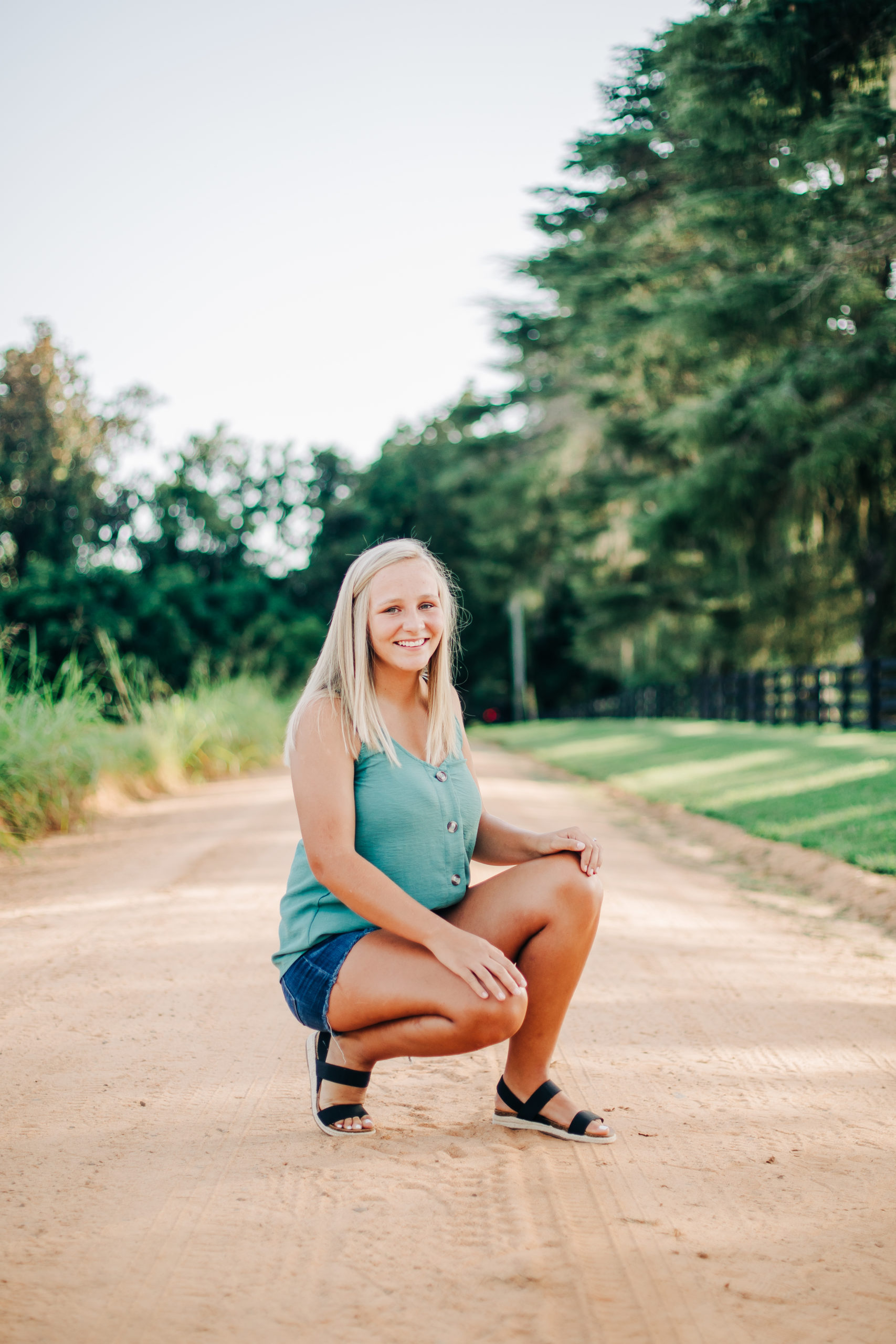 senior photos with girl crouching on a dirt path in the country for outdoor photoshoot 