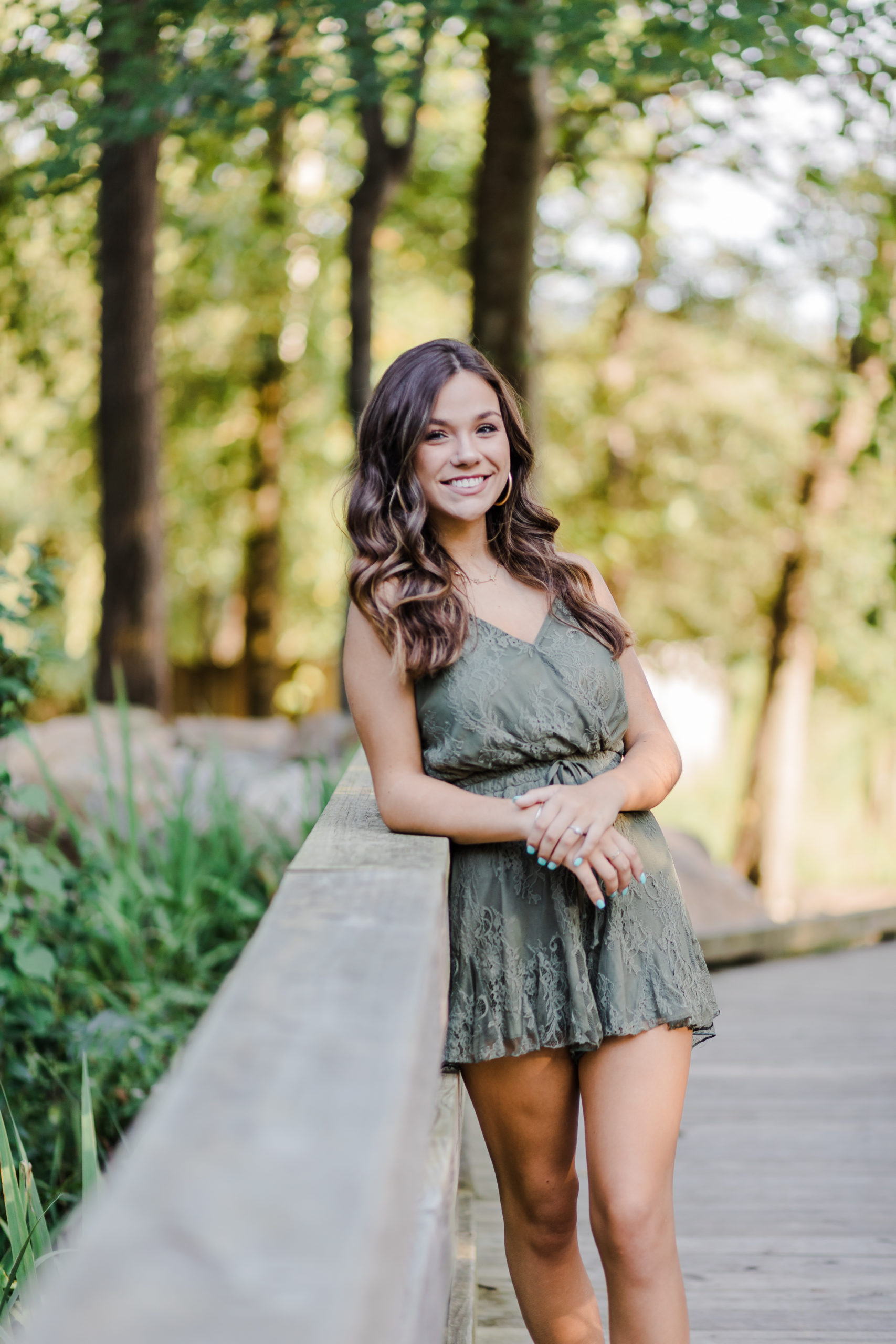 girl standing on a bridge and leaning on the railing in the woods for her senior photos in augusta