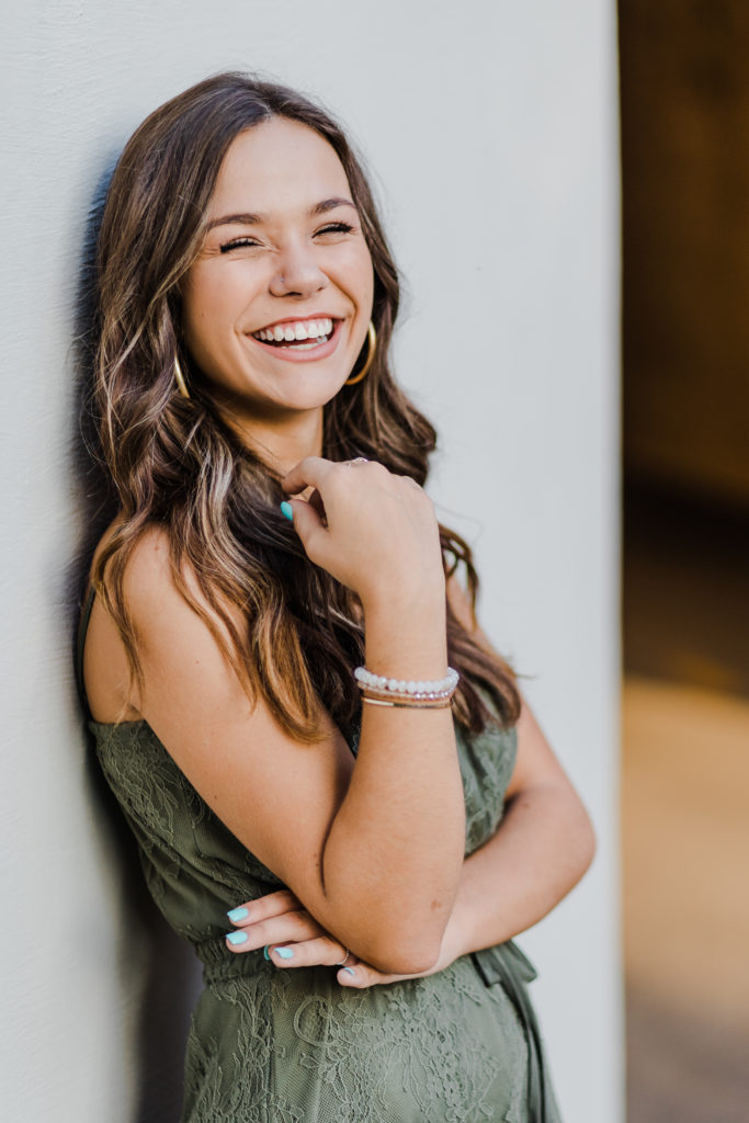 senior girl laughing while leaning against the wall for her senior pictures in Augusta