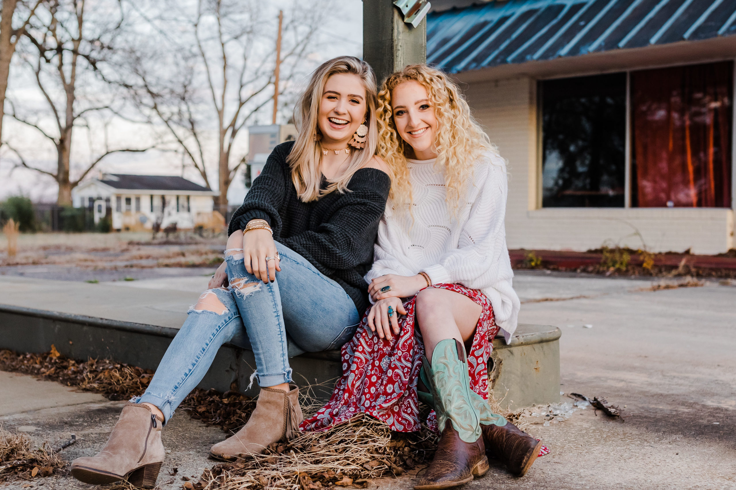 two senior girls sitting on a curb together in downtown for their senior pictures