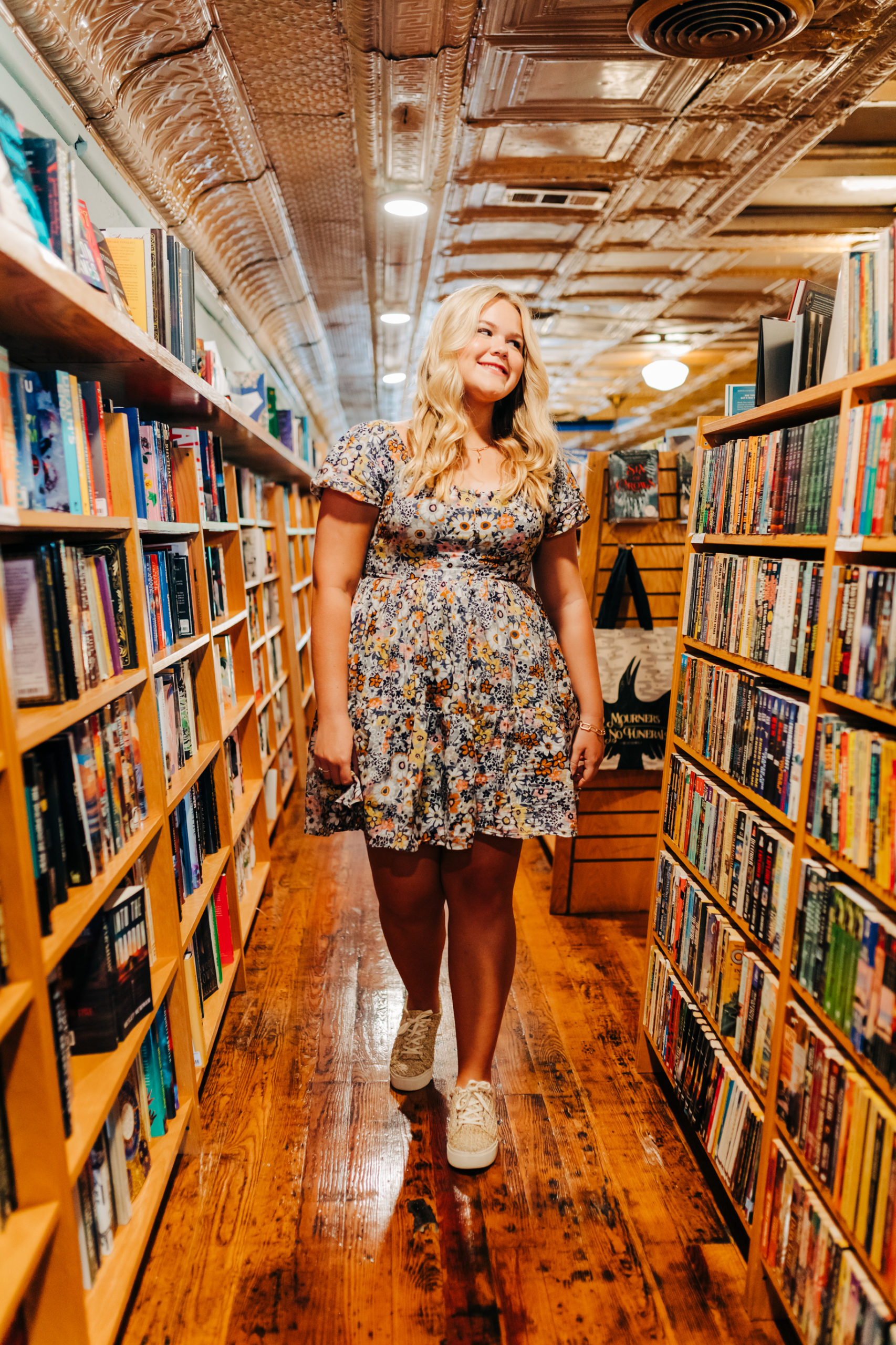 senior pictures with girl walking through a book store with book shelves on both sides of her 