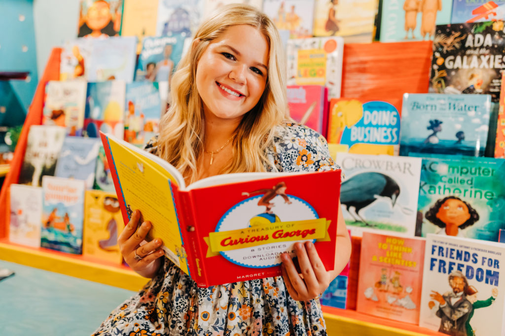 senior pictures with girl sitting on a blue bench in a book store reading a children's book 