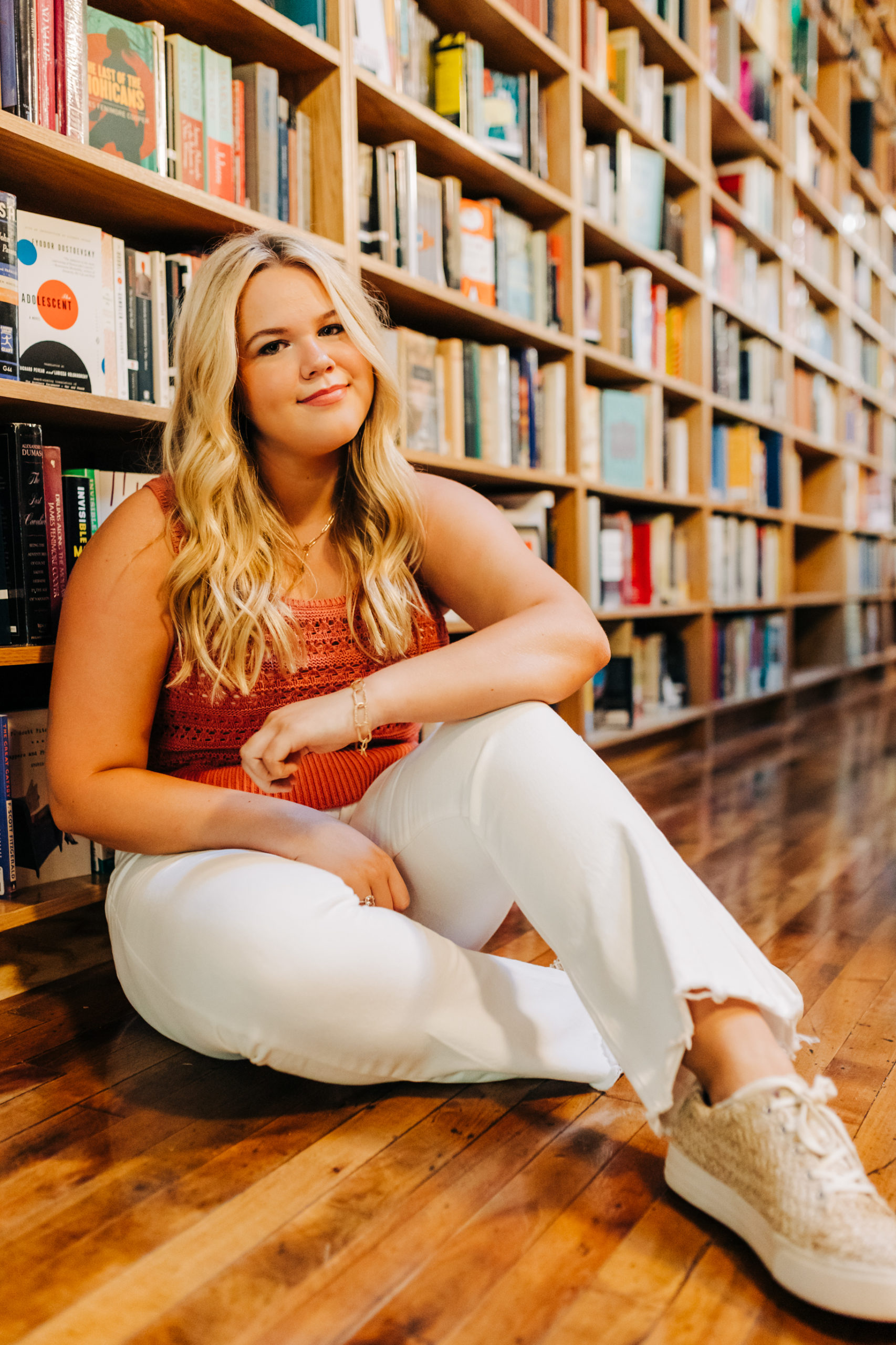 bookstore senior photos with augusta photographer as girl siting on the floor on the bookstore and smiles