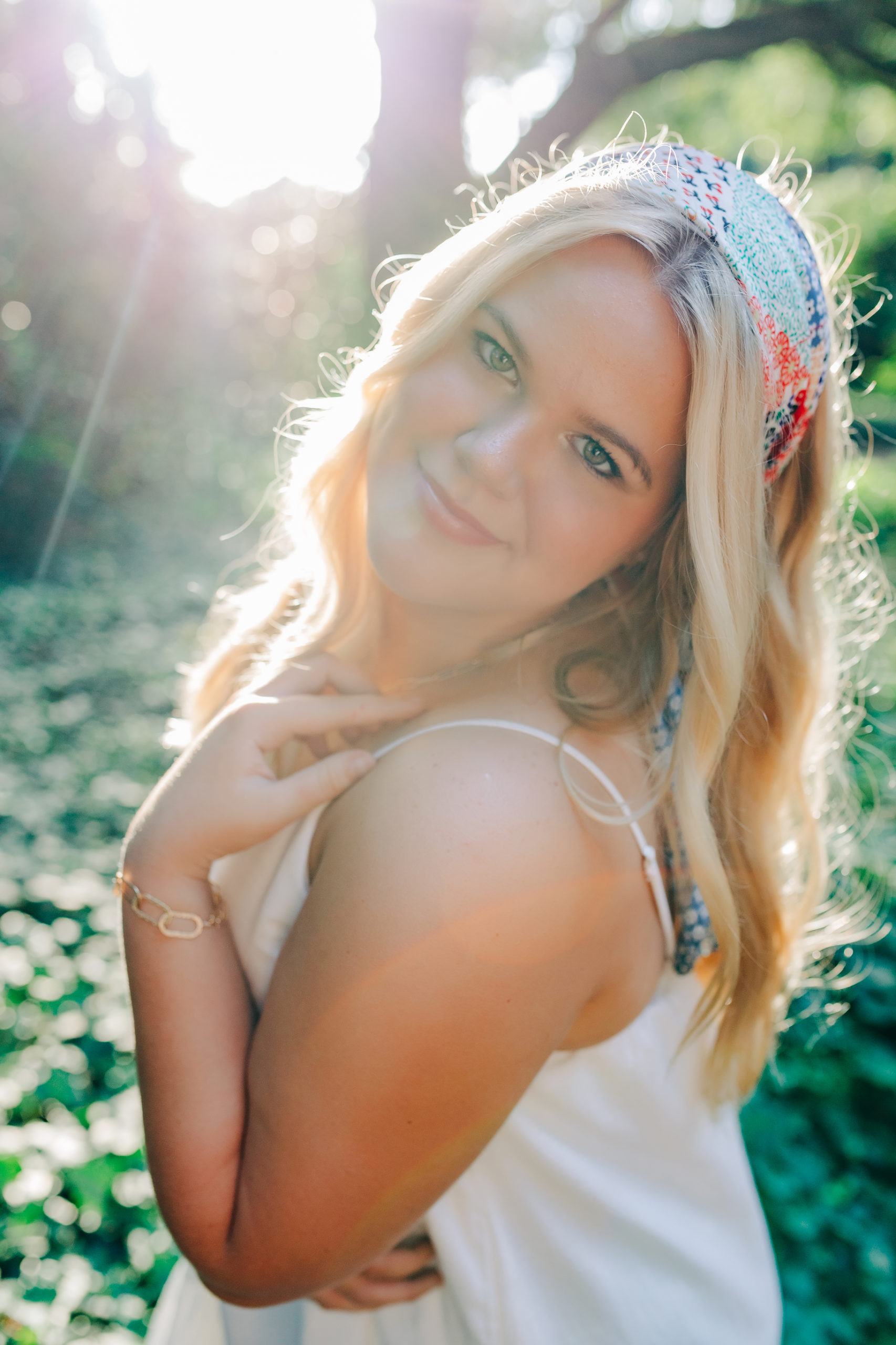 senior session in a garden in south carolina with girl in a white dress and a colorful head scarf smiling 