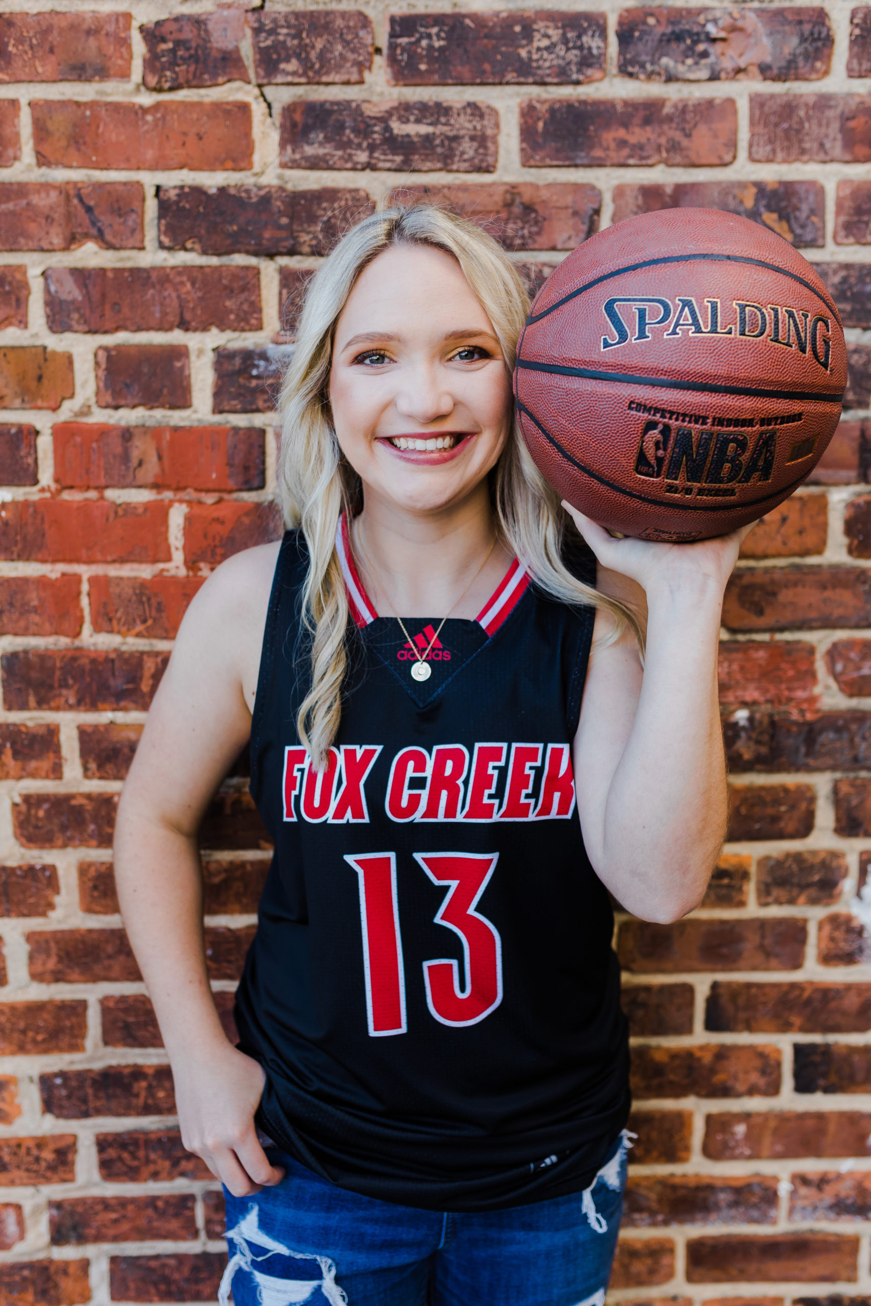 basketball player up a against a brick wall posing with a basket ball for her senior pictures