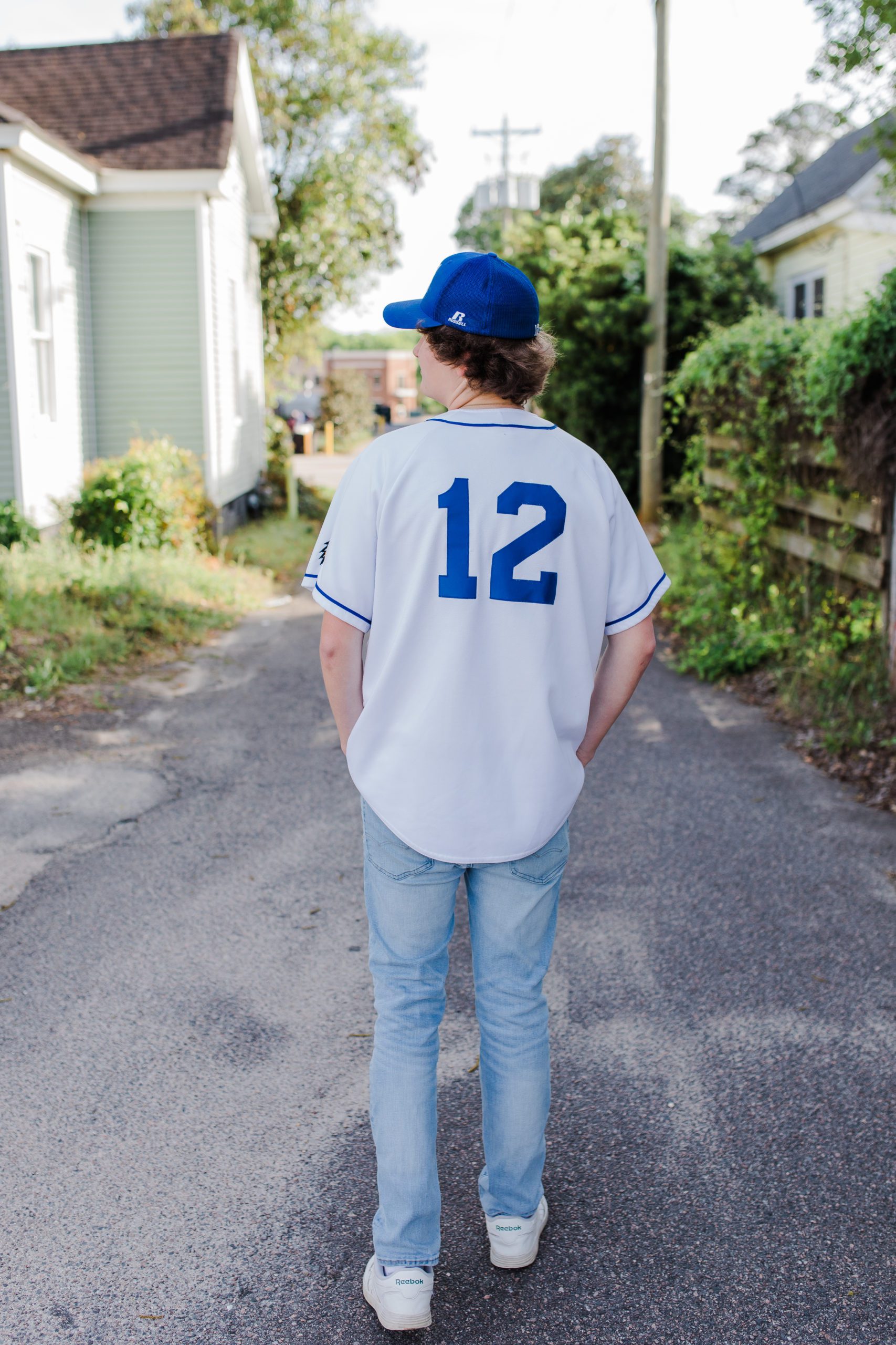 young man in a his baseball jersey walking down an alley in a small town for his seniorpictures by Augusta photographer