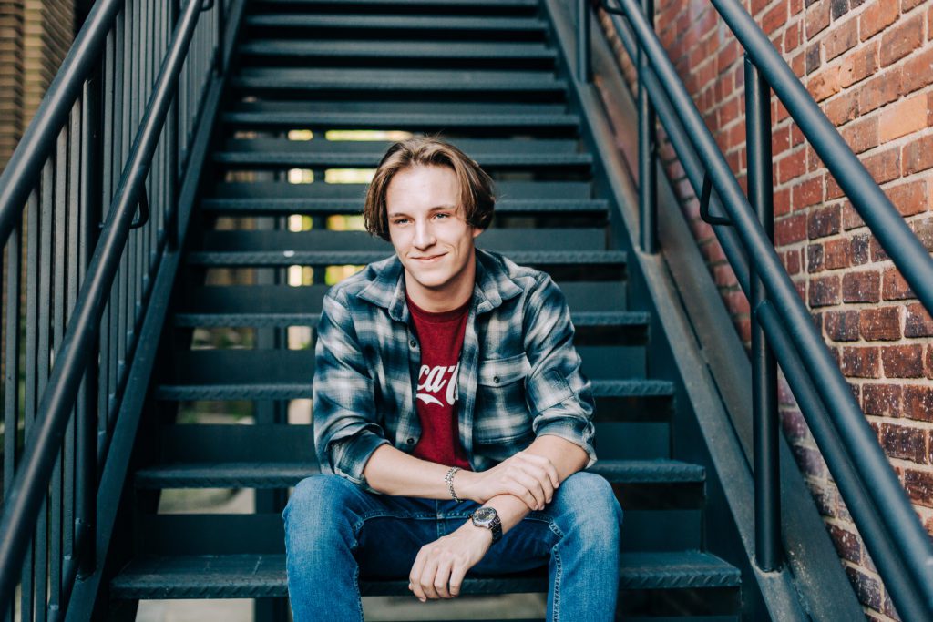 young man posing for his high school senior pictures as he sits on stairs in augusta georgia