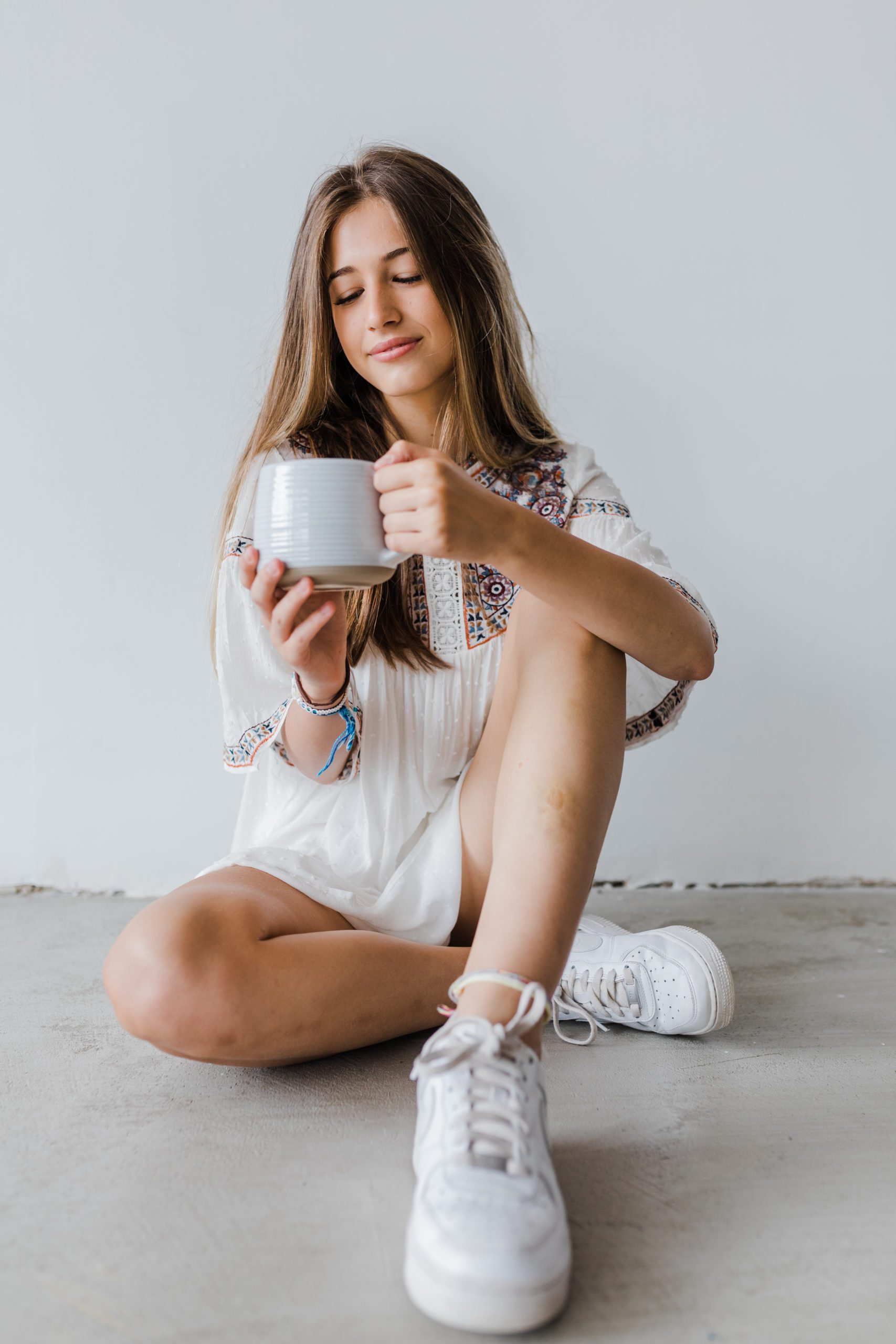 young woman sitting on the floor while holding a mug for her indoor senior pictures