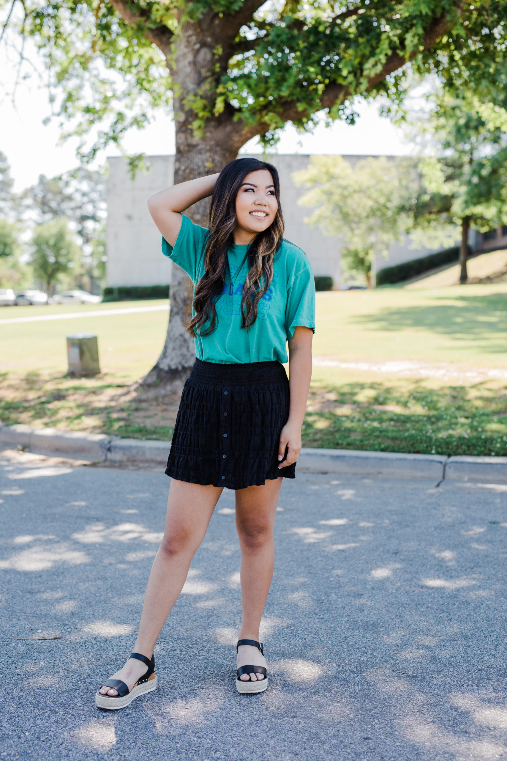 senior photo Augusta photographer captures senior girl posing outside of her school in a garden as she wears a green top and black skirt