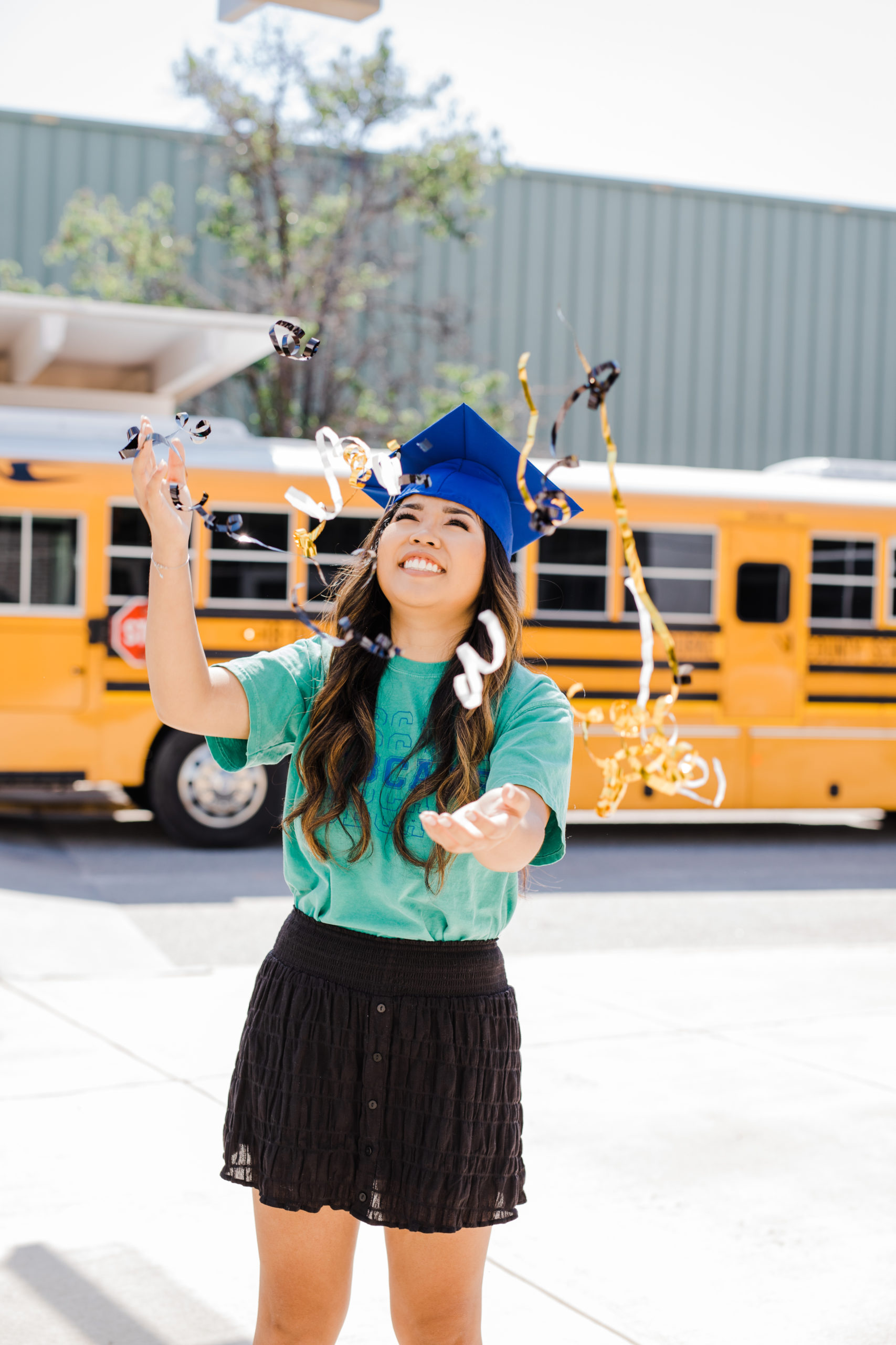 girl throwing confetti in the air with a school bus behind her for her senior photos