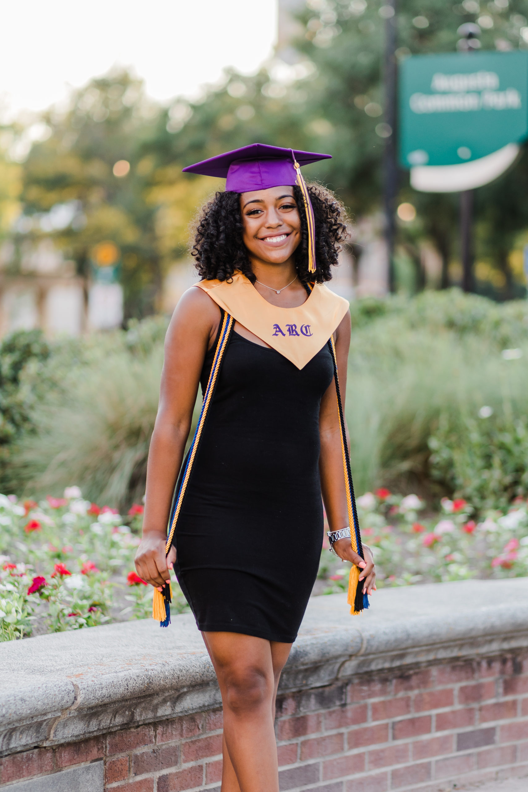 young woman in a black dress and a purple cap for her senior pictures in the campuses gardens