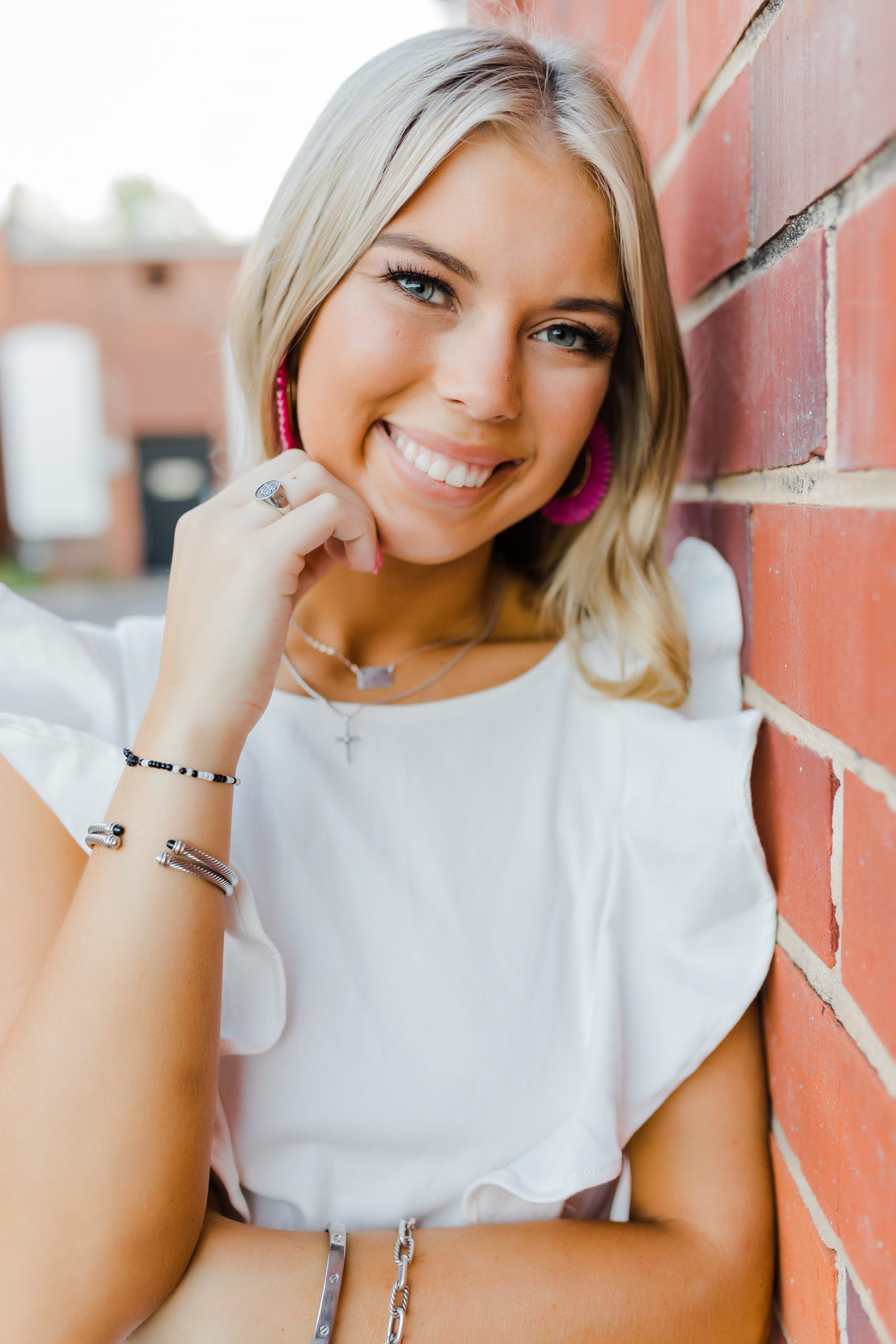senior pictures with girl leaning against a brick wall and smiling for her senior photos with Augusta photographers
