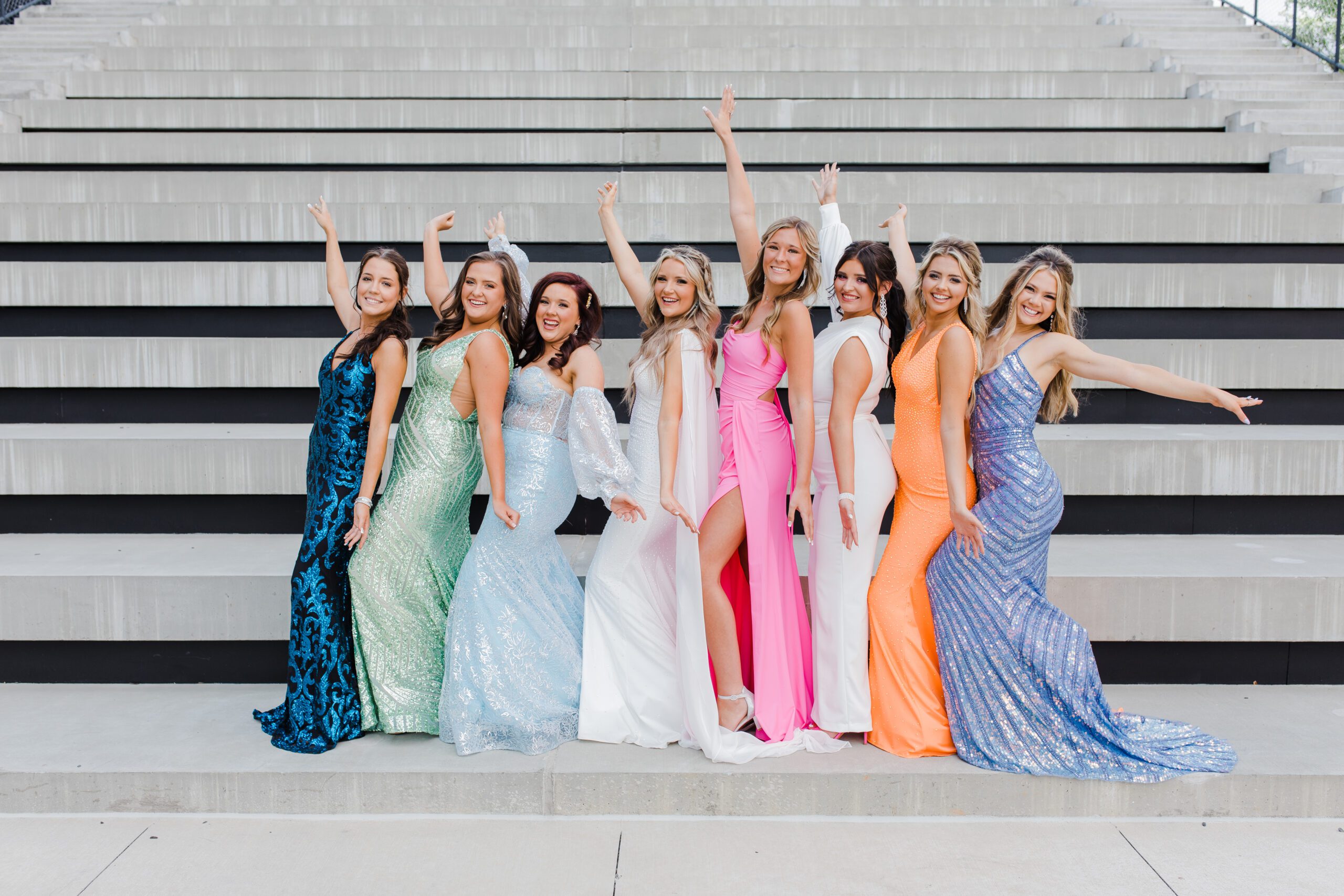 Augusta photographers photographs best friends in their prom dresses standing together in front of bleachers with their arms in the air