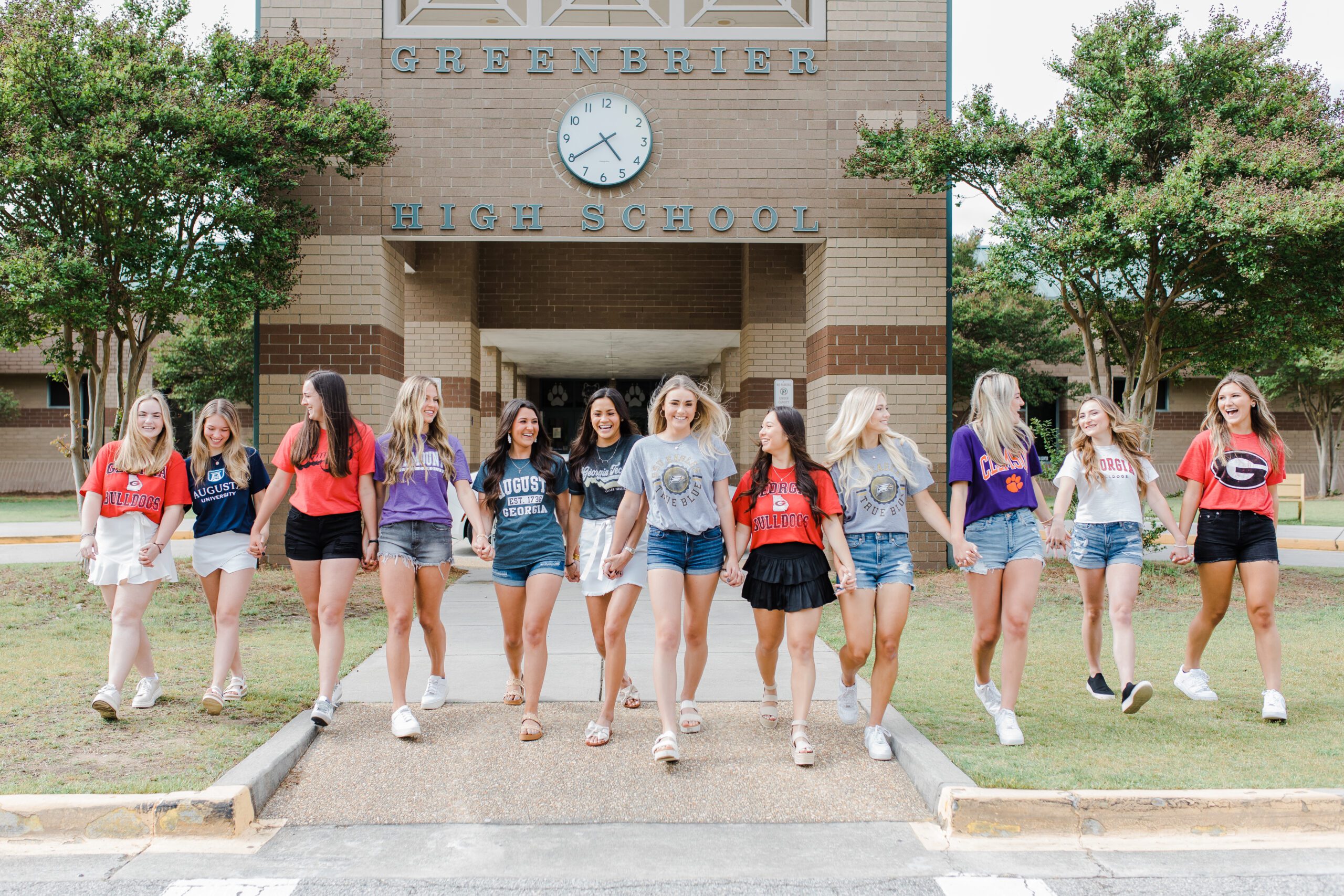 Group of friends in their senior T-shirts walking out of their high school in the front lawn captured by Augusta photographer for senior pictures